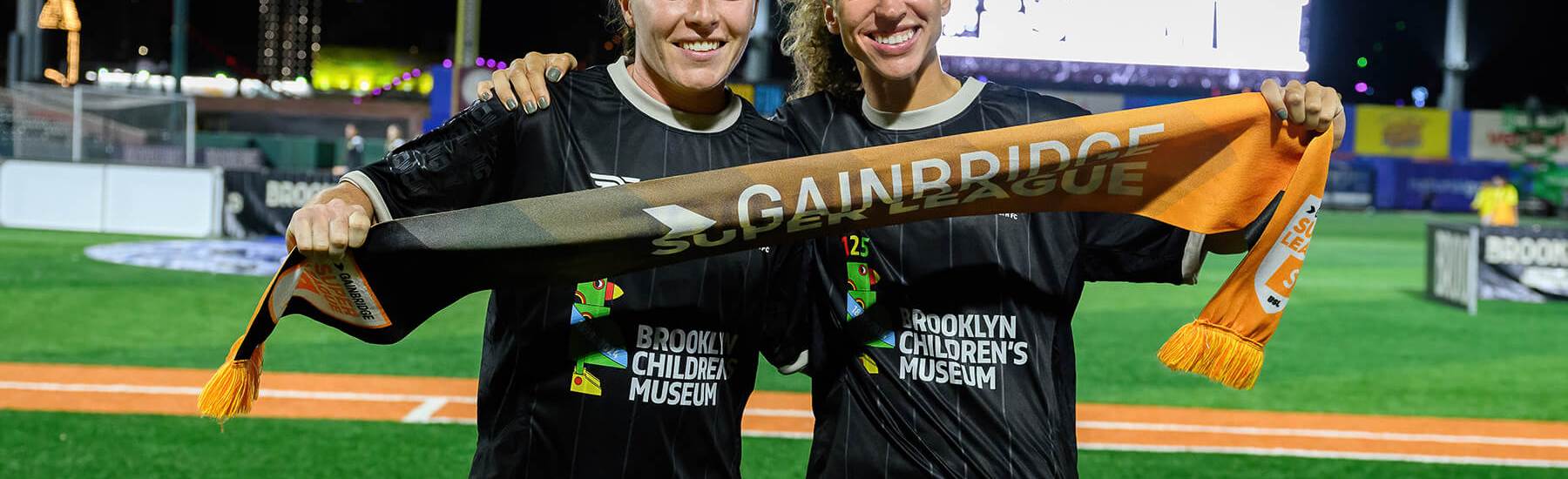 Catherine Zimmerman and Allison Williams hold a Gainbridge Super League banner after Brooklyn's 2-1 win over Tampa Bay on August 23, 2025