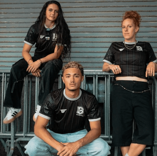 Three young people posing on a modern background wearing brooklyn fc merch