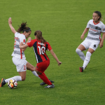 Three women compete for a ball on a soccer pitch
